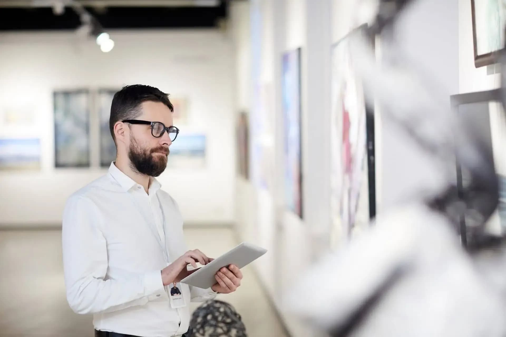 Museum manager reviewing content on a tablet in front of the works in a gallery