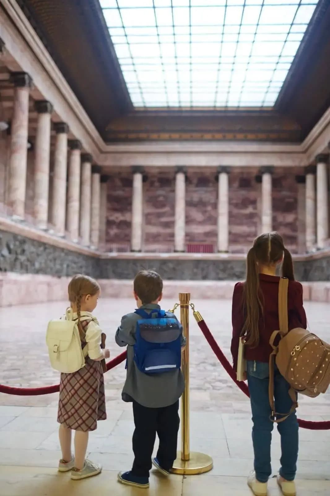 Niños con mochilas frente a una gran sala de columnas clásicas