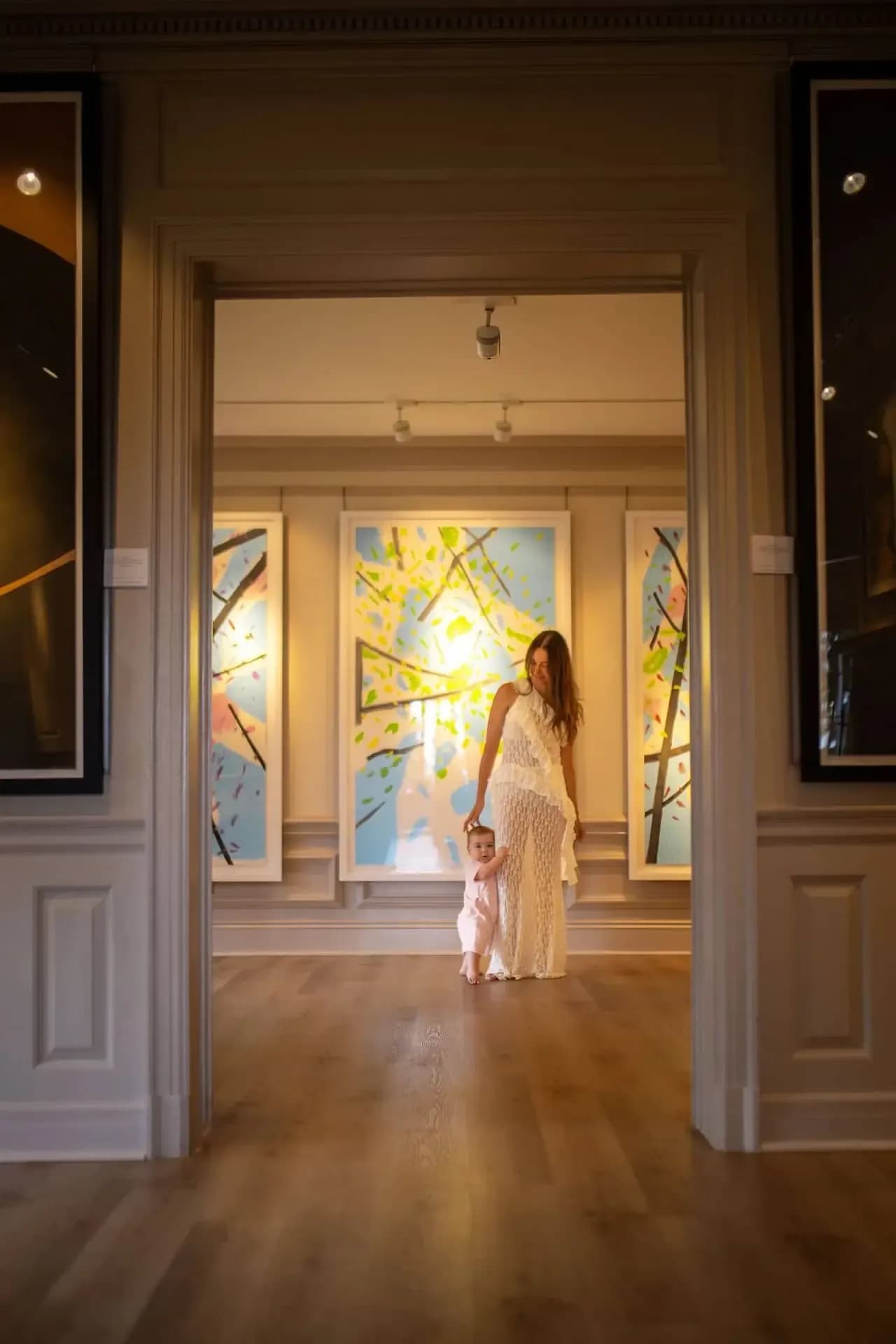 Mother and young daughter walking through a gallery with colourful paintings